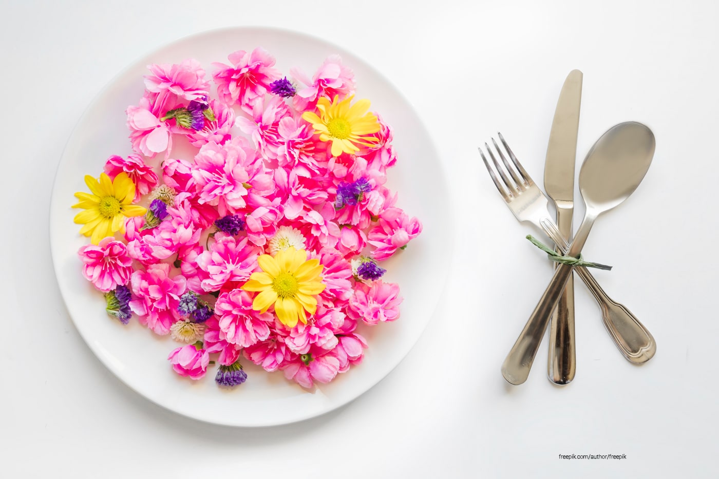 A plateful of edible flowers beside are kitchen utensils