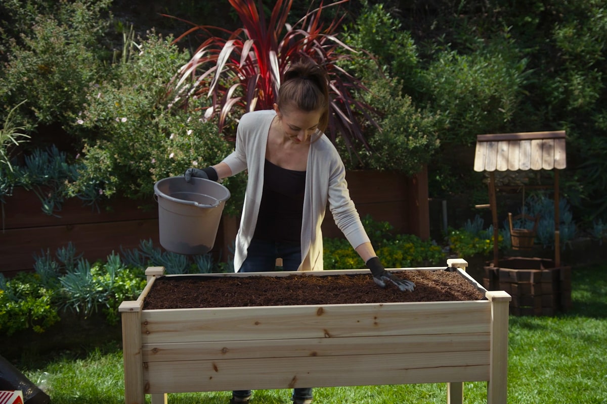 A woman putting soil in her raised bed garden